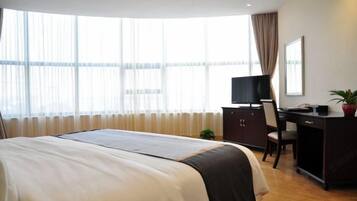 A hotel room with a bed, a desk, a chair, a television, and a window with curtains.