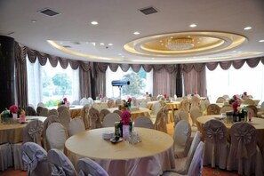 Une salle de banquet avec des tables rondes, des chaises et un lustre.