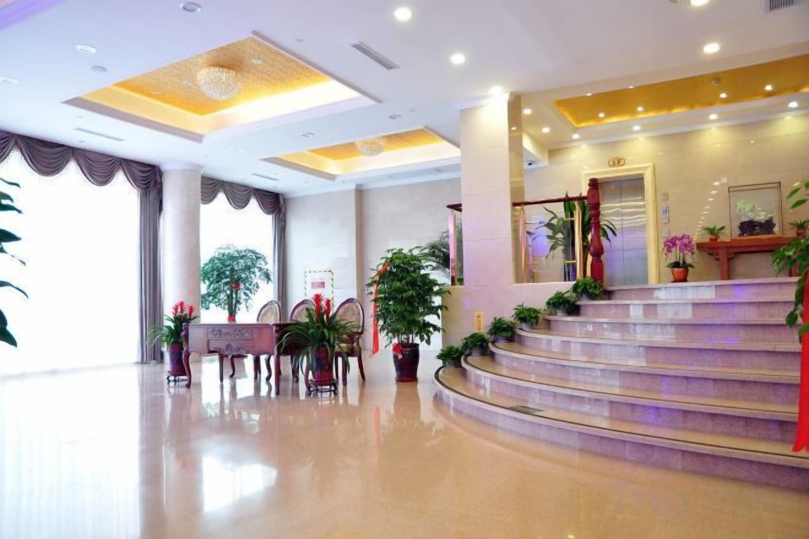 A hotel lobby with a reception desk, a staircase, and potted plants.