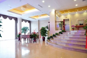 A hotel lobby with a reception desk, a staircase, and potted plants. - Shenhang Yinju Mingzhu Hotel (Jiashan)