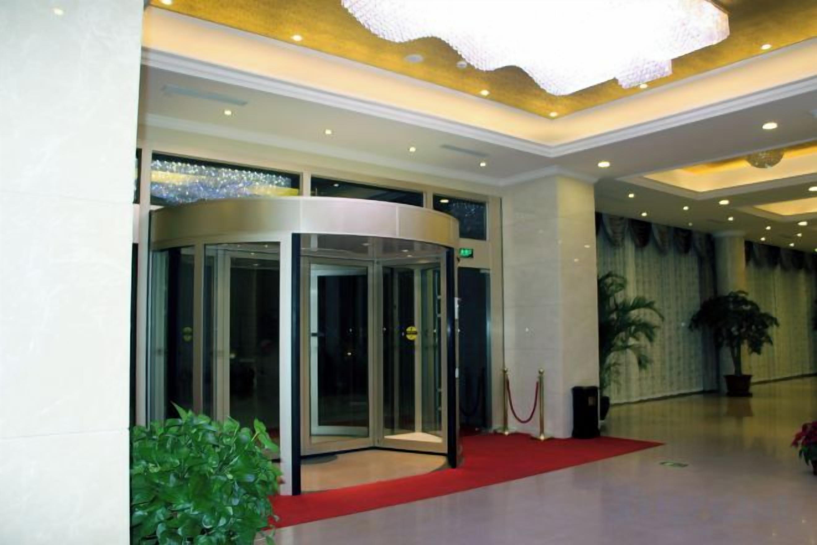 A hotel lobby with a revolving door, a red carpet, and a large potted plant.
