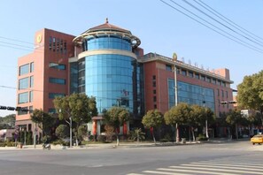 A multi-story hotel with a prominent blue cylindrical section, a red facade, and a corner location with trees. - Shenhang Yinju Mingzhu Hotel (Jiashan)