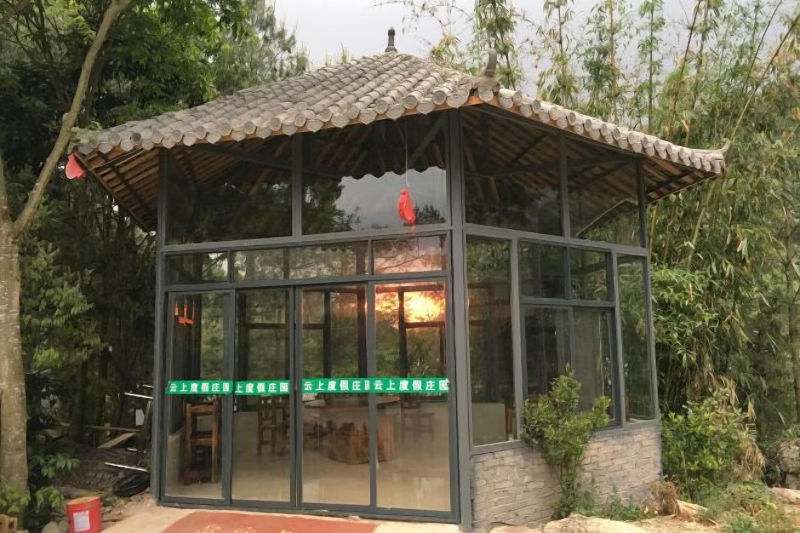 Una estructura con paredes de vidrio y techo de tejas, rodeada de vegetación.