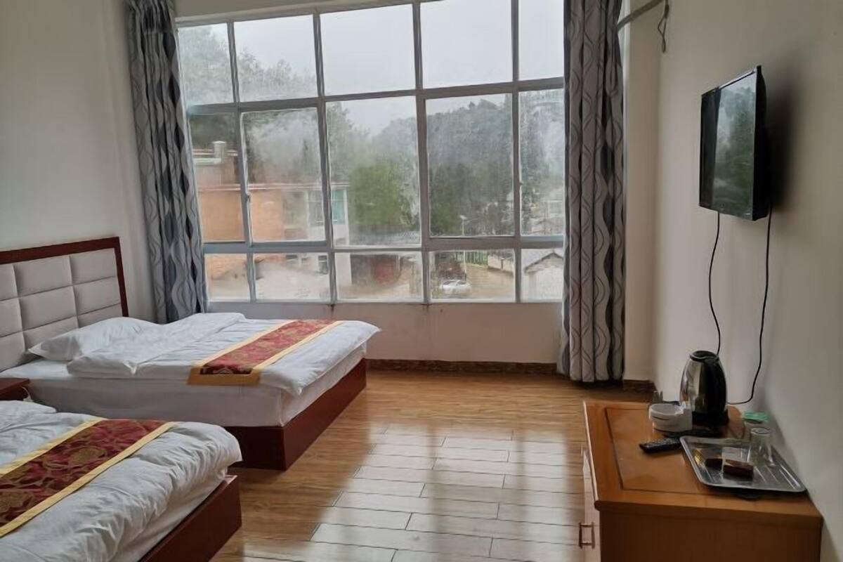 A hotel room with two beds, a TV, a coffee maker, and a window with a view of the outside.