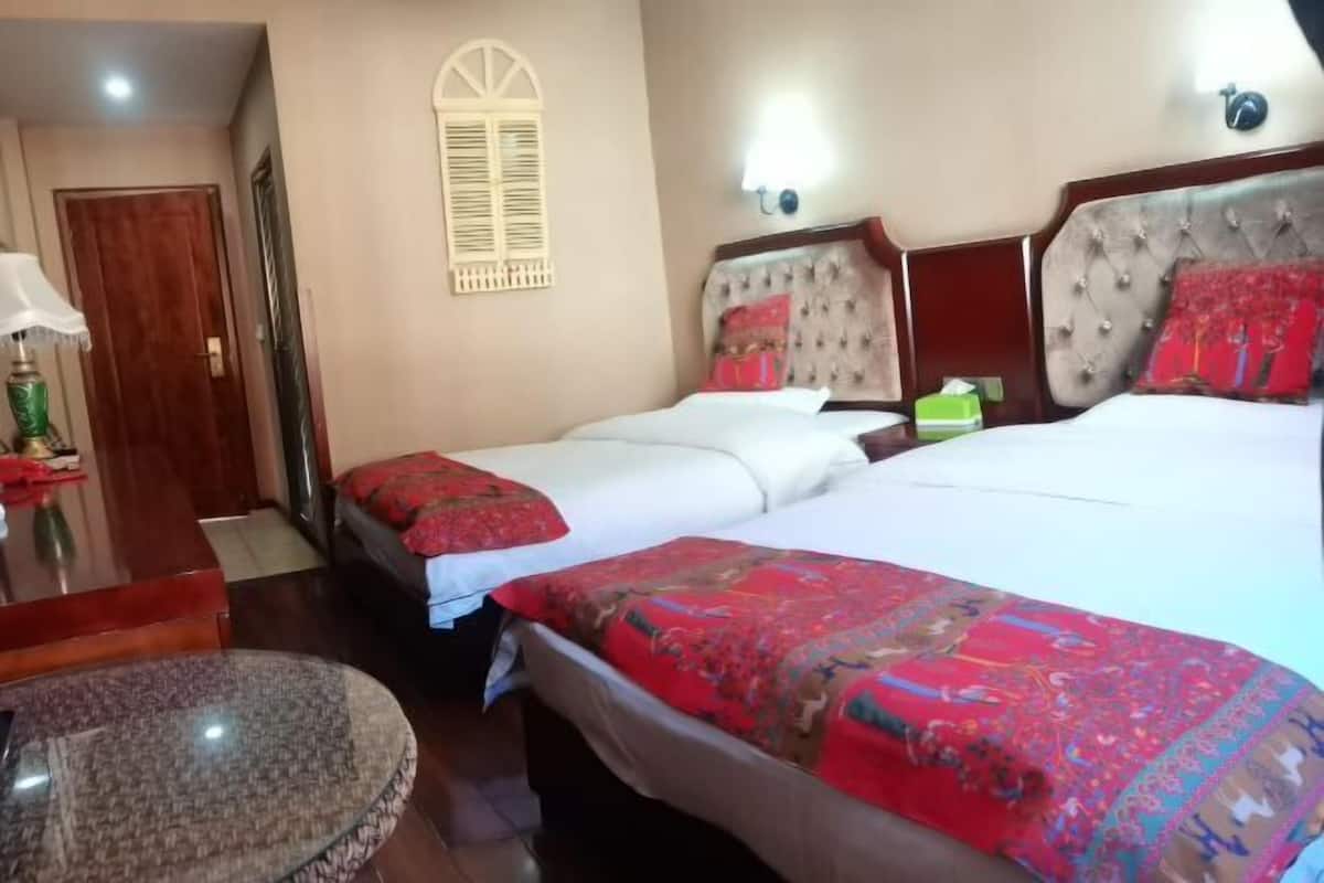 Une chambre d’hôtel avec deux lits, une table ronde, un bureau en bois et une lampe.