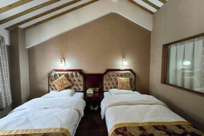 A room with two beds, each with a headboard and a pillow. There are wall-mounted lights above the beds, and a window on the right side.