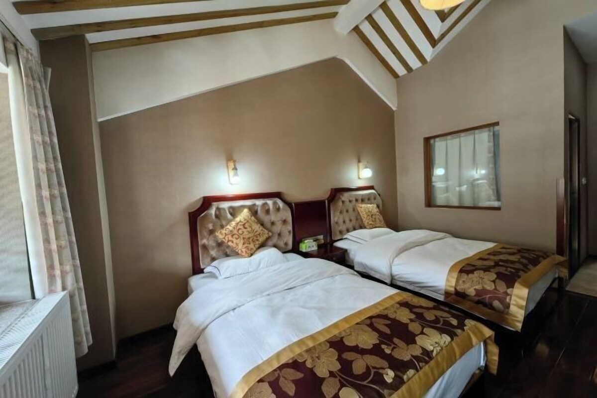 A hotel room with two single beds, a wooden ceiling, and a window with blinds.