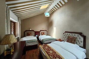 A hotel room with two single beds, wooden flooring, a ceiling with wooden beams, and a small table with a lamp.