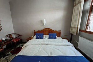 A bedroom with a wooden bed, white bedding, a nightstand, a chair, and a window with curtains.