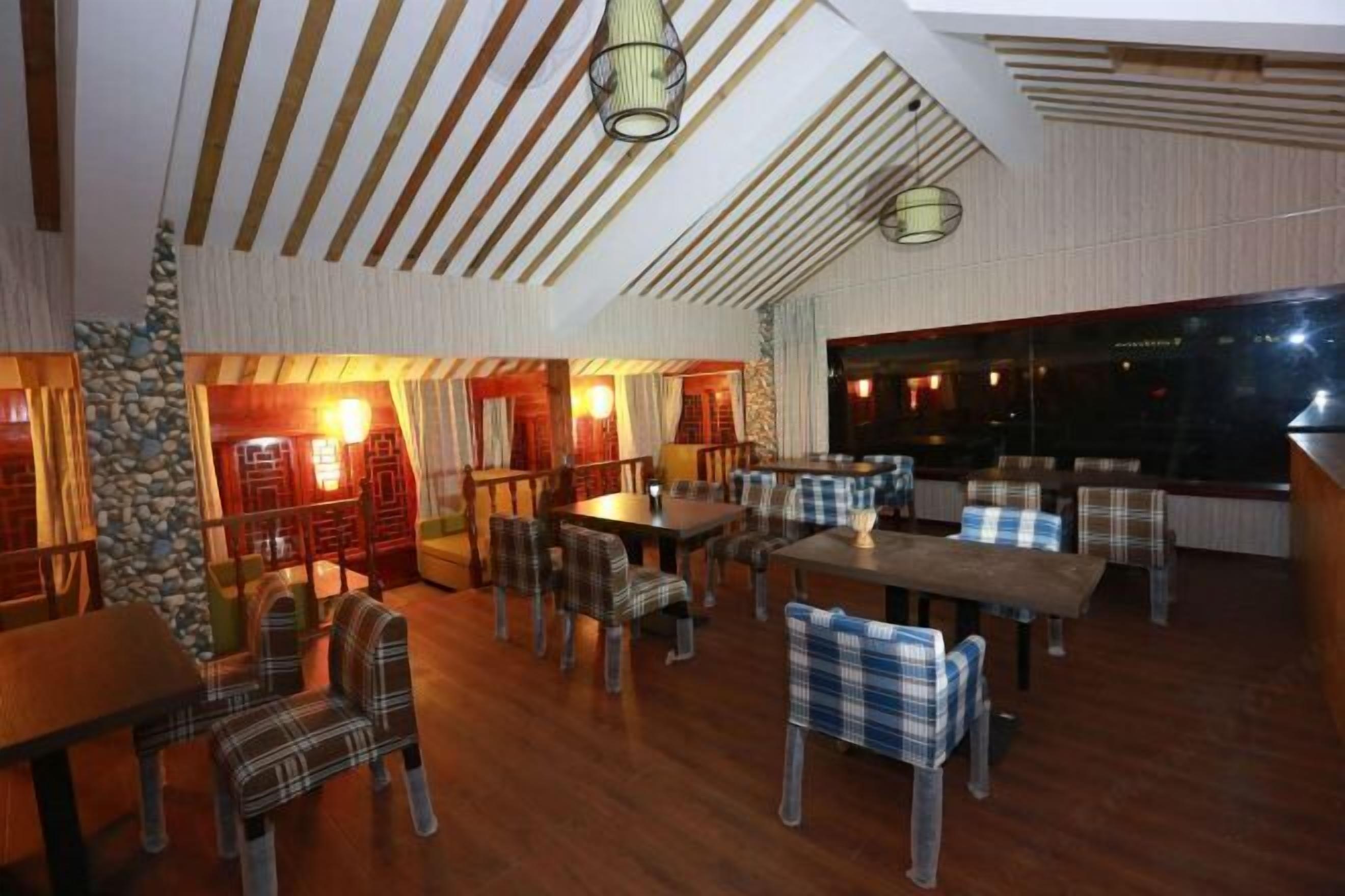 Ein Restaurant mit Holzböden, karierten Stühlen und Tischen. Hängelampen und eine Steinwand sind vorhanden.