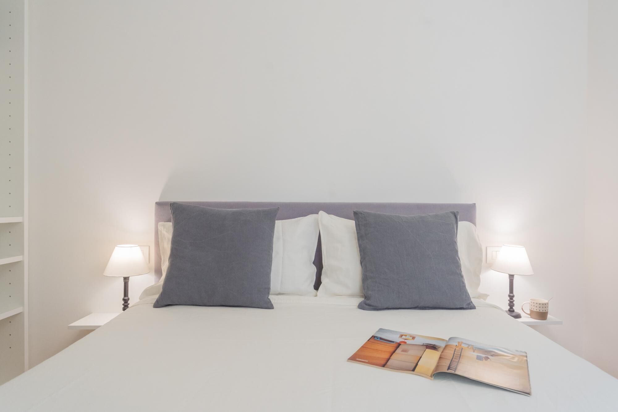 Una cama bien tendida con dos almohadas, una revista sobre la cama y dos lámparas de noche.