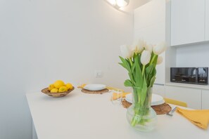 Eine Küche mit weißen Schränken, einer Mikrowelle, einer Zitronenschale, einer Vase mit weißen Blumen und einer gelben Serviette.