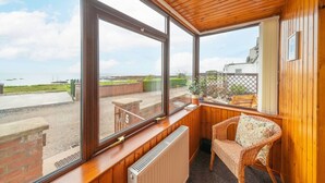 Ein gemütliches Zimmer mit Holzwänden und großen Fenstern mit Blick auf das Meer und eine Rasenfläche.