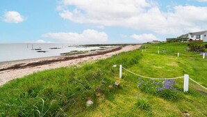 Eine Küstenlandschaft mit einem grasbewachsenen Weg, der zum Strand führt, einem weißen Zaun und einem Gebäude im Hintergrund.