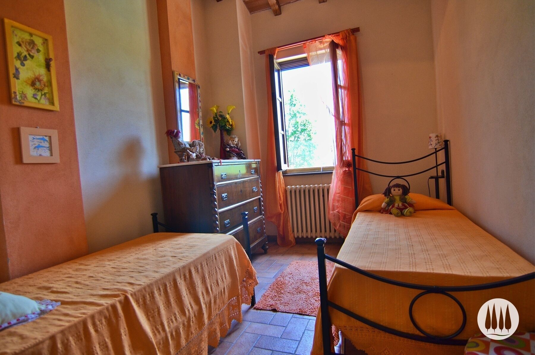 A bedroom with two single beds, a dresser, a radiator, and a window with curtains.