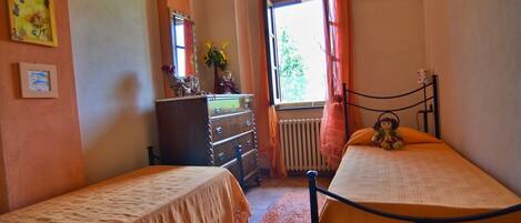 A bedroom with two single beds, a dresser, a radiator, and a window with curtains.