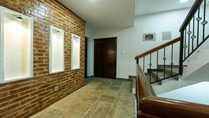 A hallway with a brick wall, three illuminated panels, a wooden staircase, and a door. - MeroStay 161 SN HOTEL (Lalitpur)