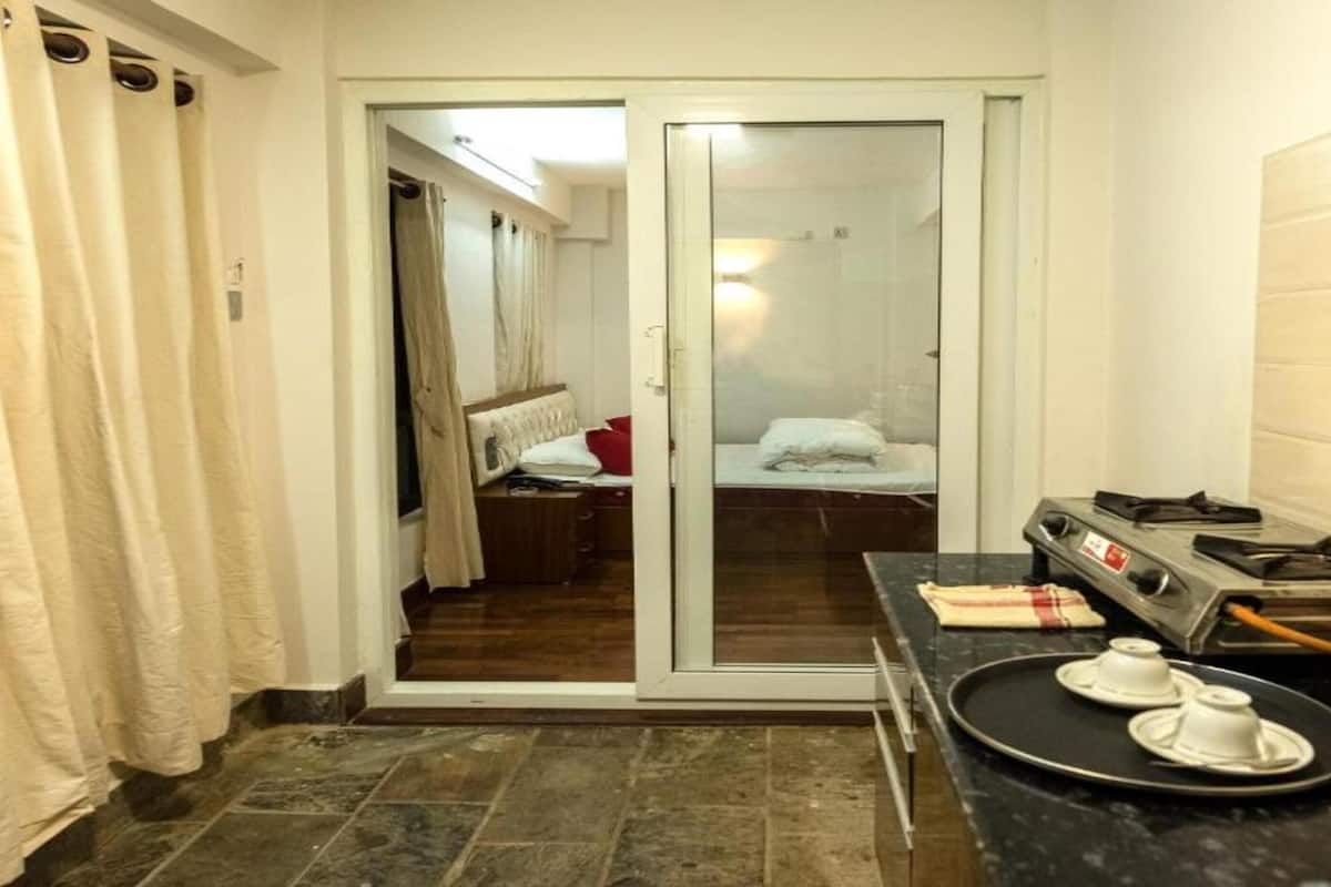 Een compacte hotelkamer met een schuifdeur naar een slaapkamer. De kamer heeft een kitchenette met een fornuis, waterkoker en een dienblad met bekers.