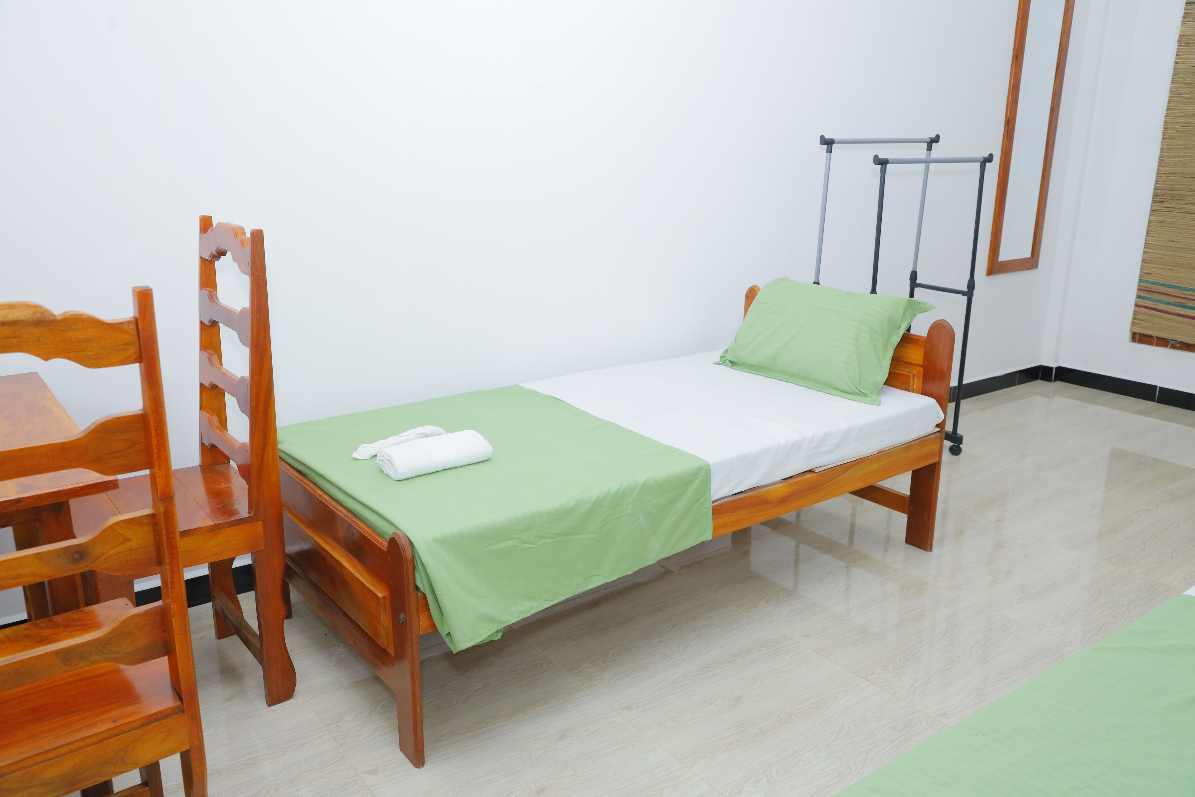 Una cama individual con una colcha verde y una almohada blanca, una silla de madera y una mesita.