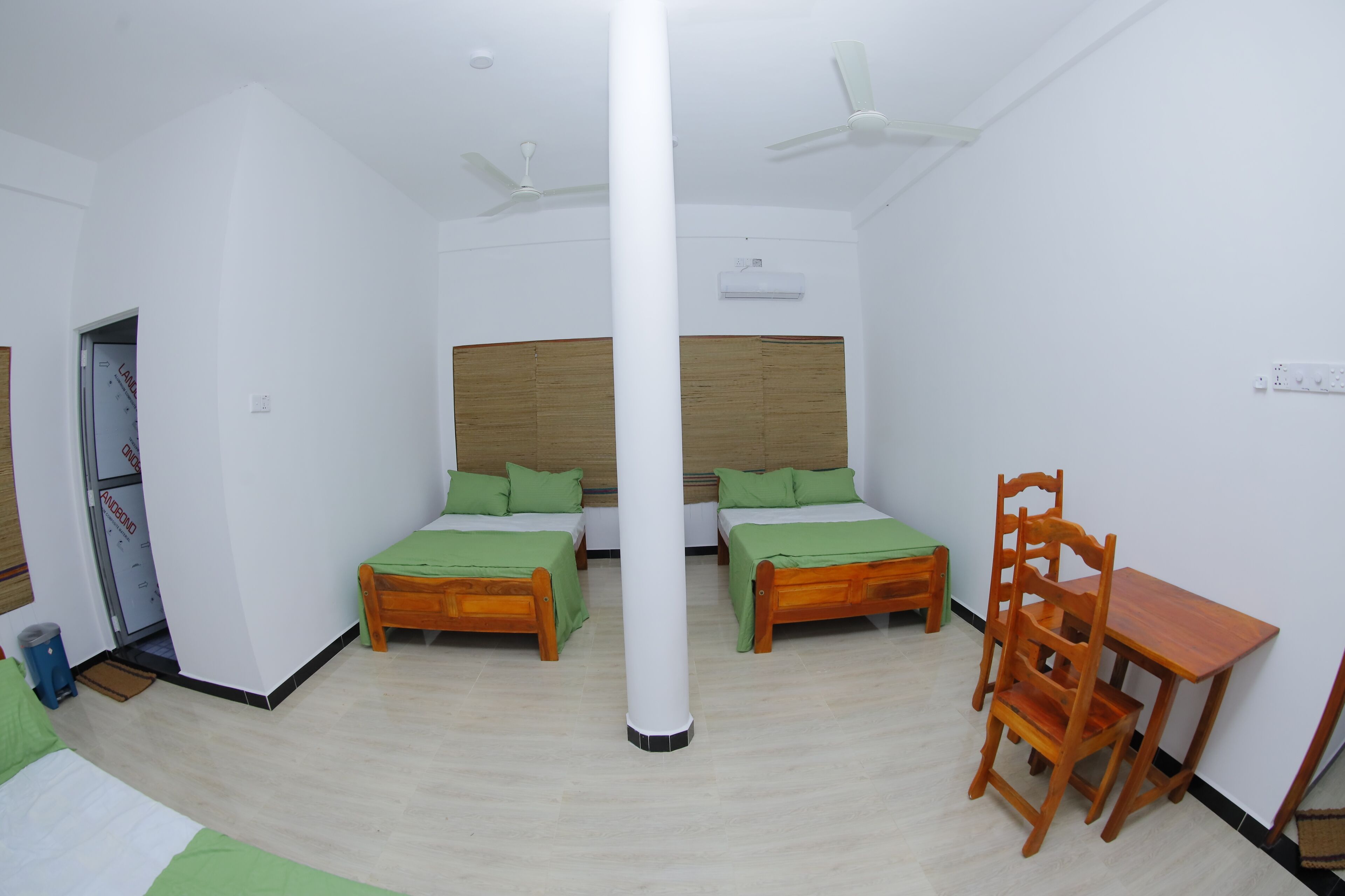 Een kamer met twee houten bedden, een houten tafel, een stoel, een plafondventilator en een airconditioning.