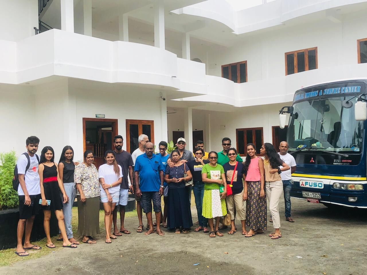 A group of people standing in front of a building with a bus parked nearby.