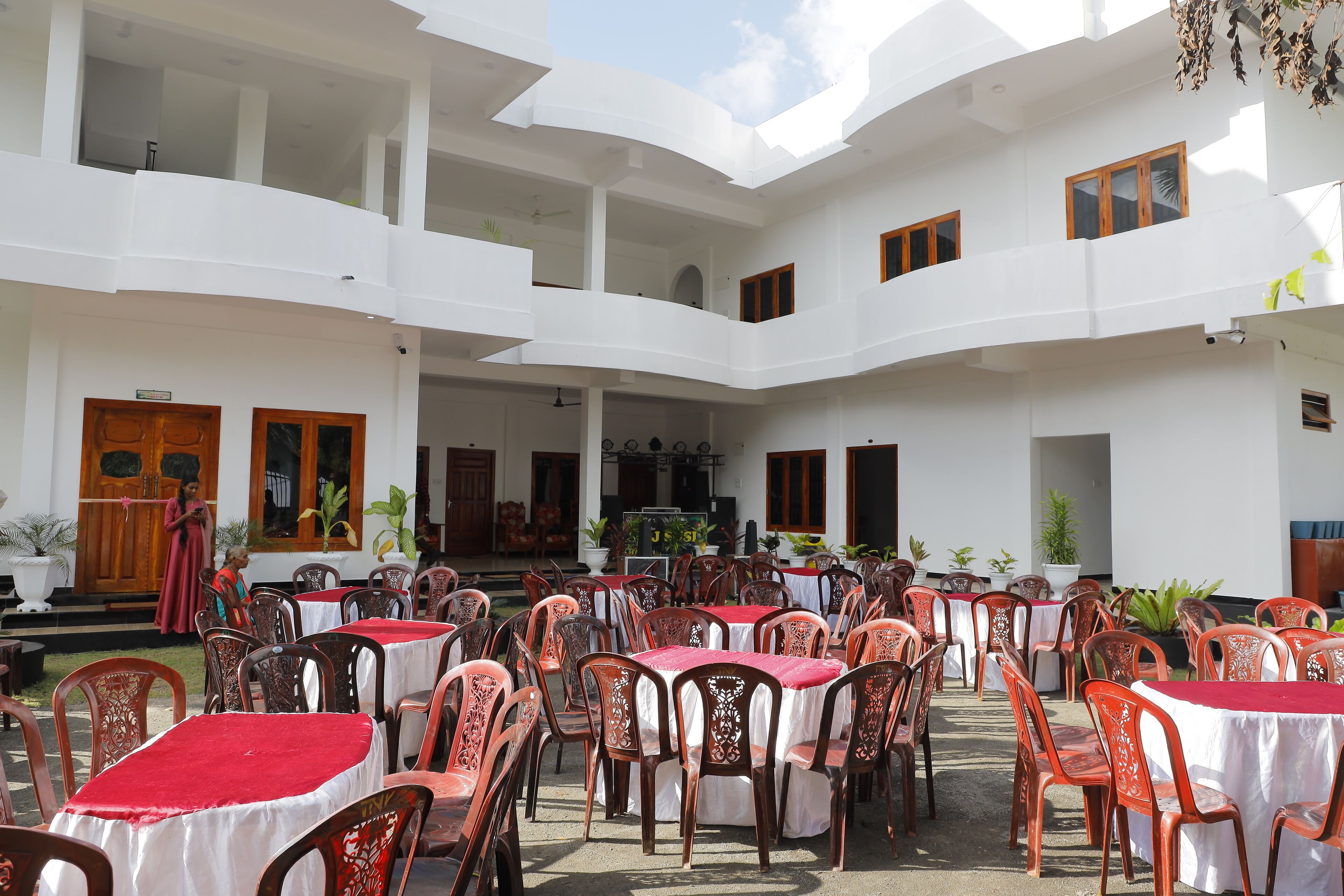 A courtyard with multiple tables and chairs, a stage, and a white building with balconies.