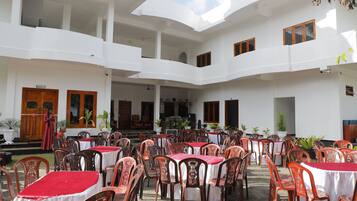 A courtyard with multiple tables and chairs, a stage, and a white building with balconies.