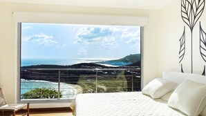A bedroom with a large window offering a view of the ocean and hills. - Numa Indigo BAY (INDIGO BAY)