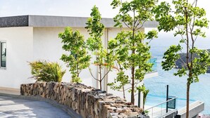 A modern building with a stone retaining wall, a pool, and a view of the ocean. - Numa Indigo BAY (INDIGO BAY)