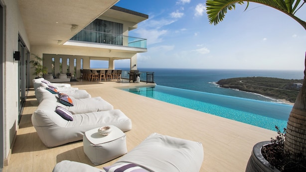 A modern outdoor pool area with white lounge chairs and a dining area overlooking the ocean. - Numa Indigo BAY (INDIGO BAY)