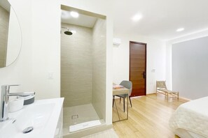 A modern bathroom with a shower, a sink, and a mirror. There is a wooden door and a chair in the room. - Numa Indigo BAY (INDIGO BAY)