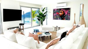 A modern living room with a white sofa, a flat-screen TV, a large window with a view of mountains, and a potted plant. - Numa Indigo BAY (INDIGO BAY)