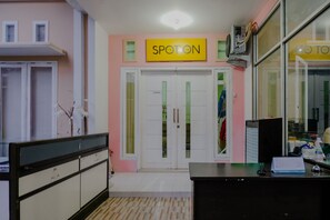 Un área de recepción con un cartel que dice "SPOTON" sobre la entrada, un mostrador con un calendario y una ventana con persianas.