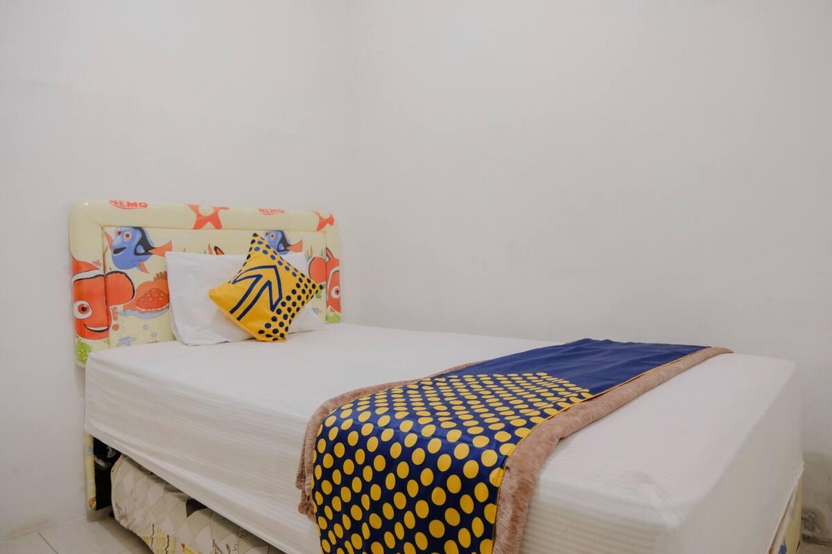 A bed with a white mattress, a blue and yellow polka dot blanket, and a pillow with a yellow and black design.