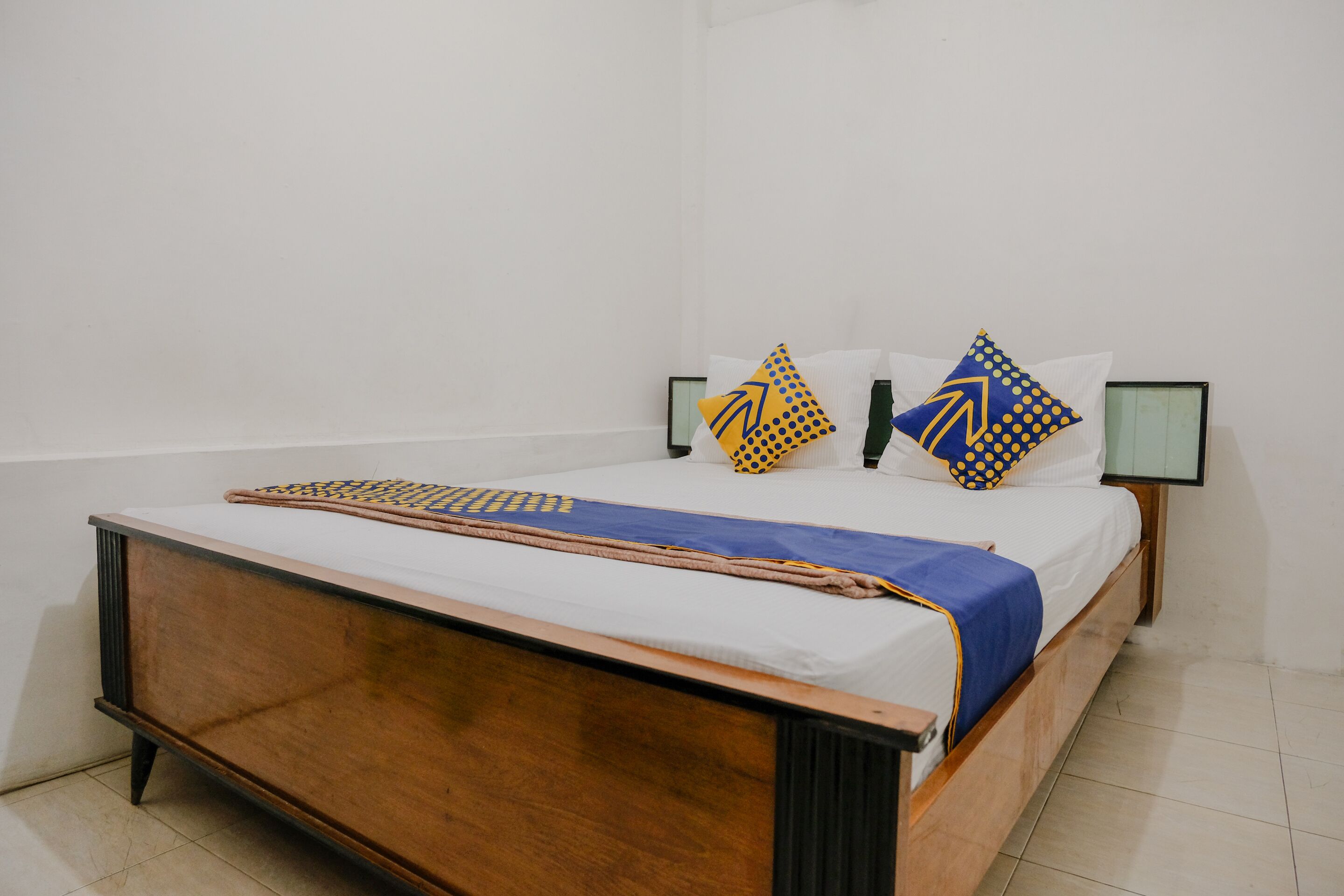 A bed with a wooden frame, white bedding, and two pillows with geometric patterns.