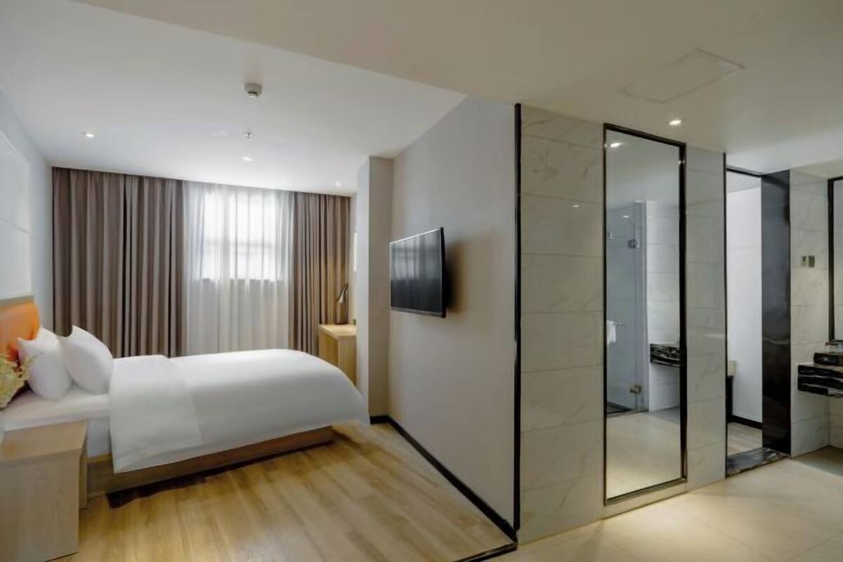 A hotel room with a bed, a TV, a bathroom with a mirror, and a wooden floor.