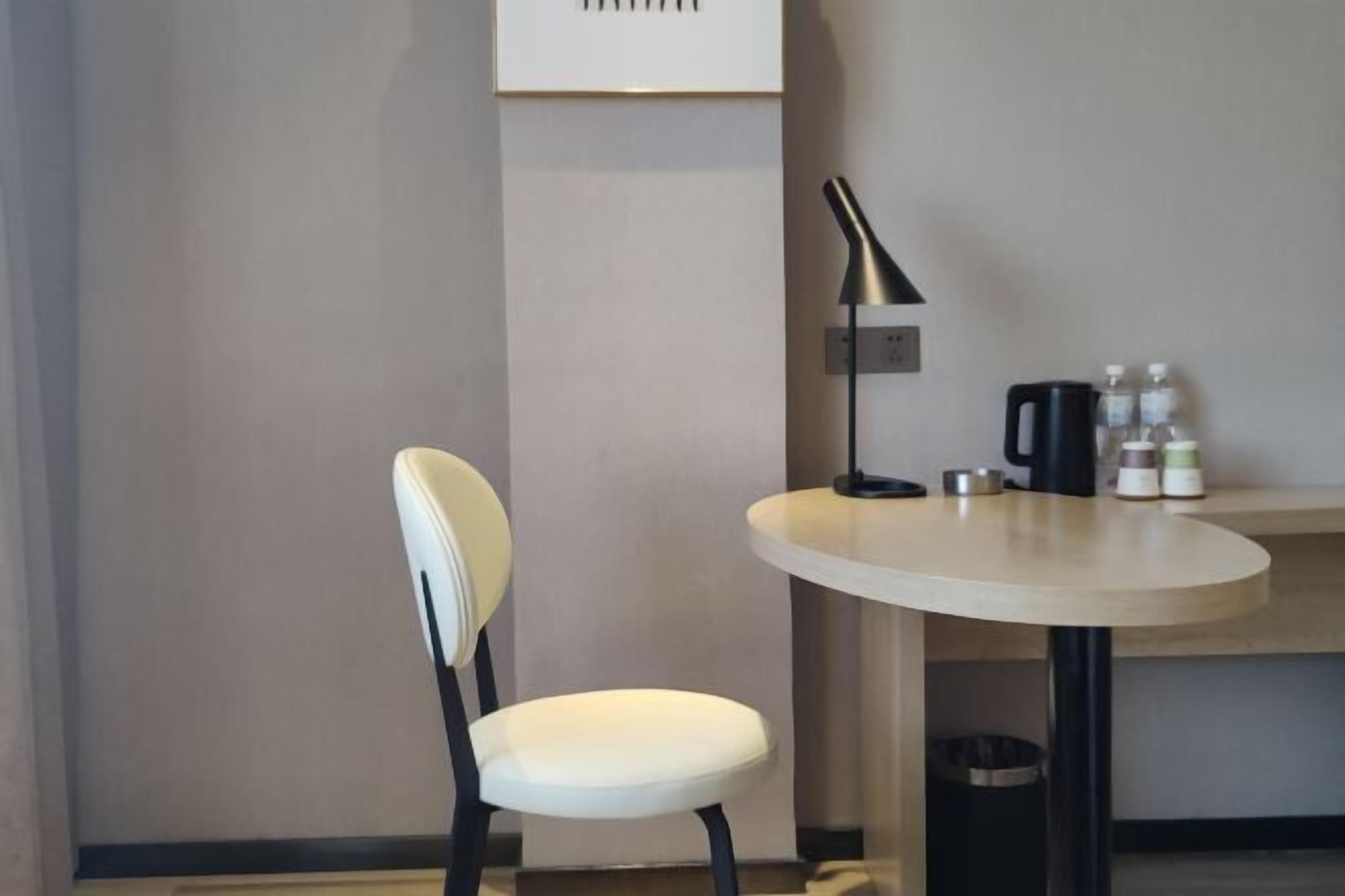 A modern room with a round table, a chair, a lamp, and a small shelf with bottles and a kettle.