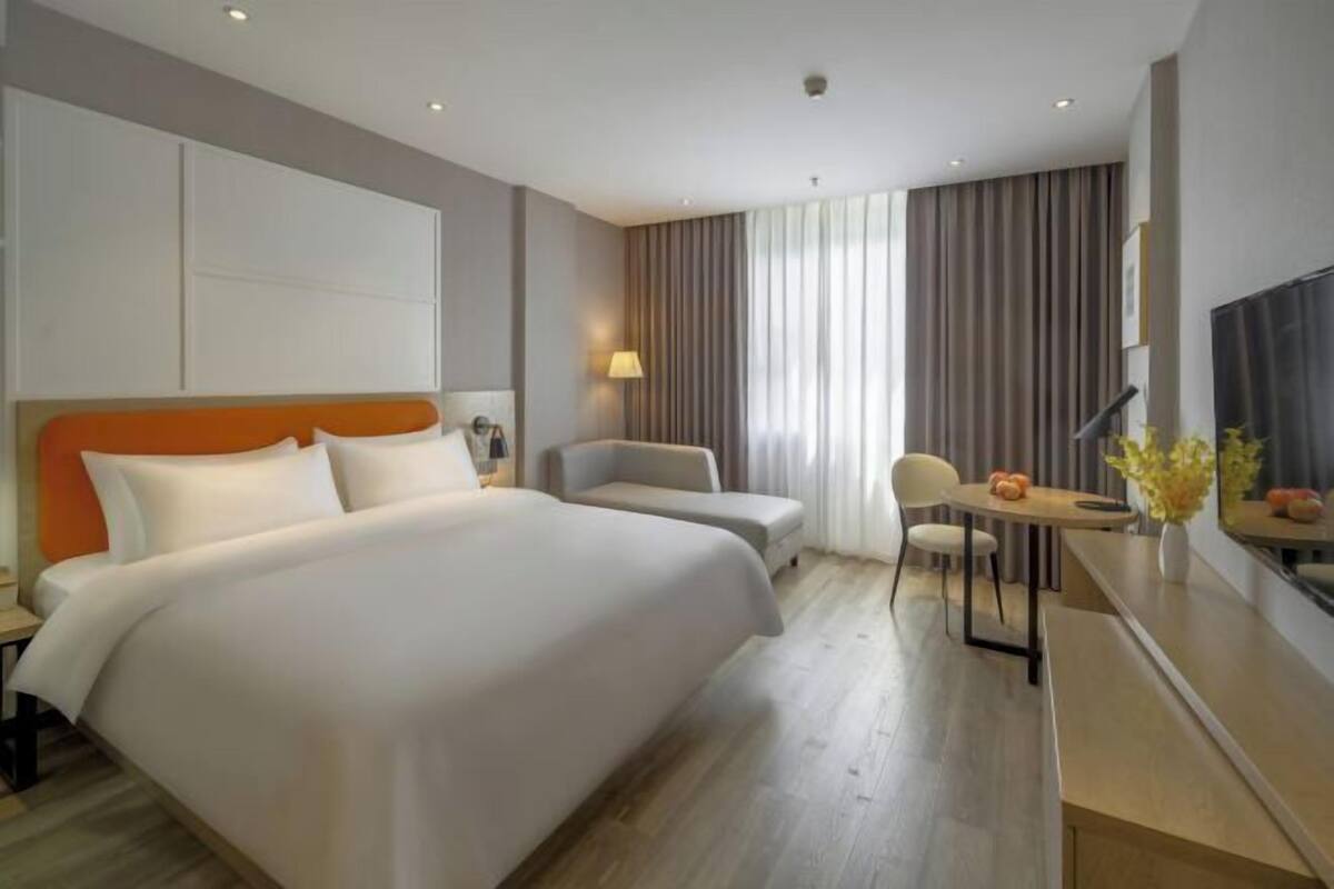 A hotel room with a large bed, a desk, a chair, and a TV.