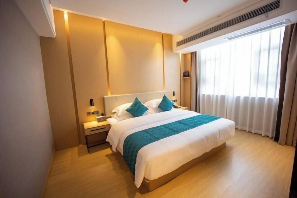 A hotel room with a bed, bedside table, and a window with curtains.