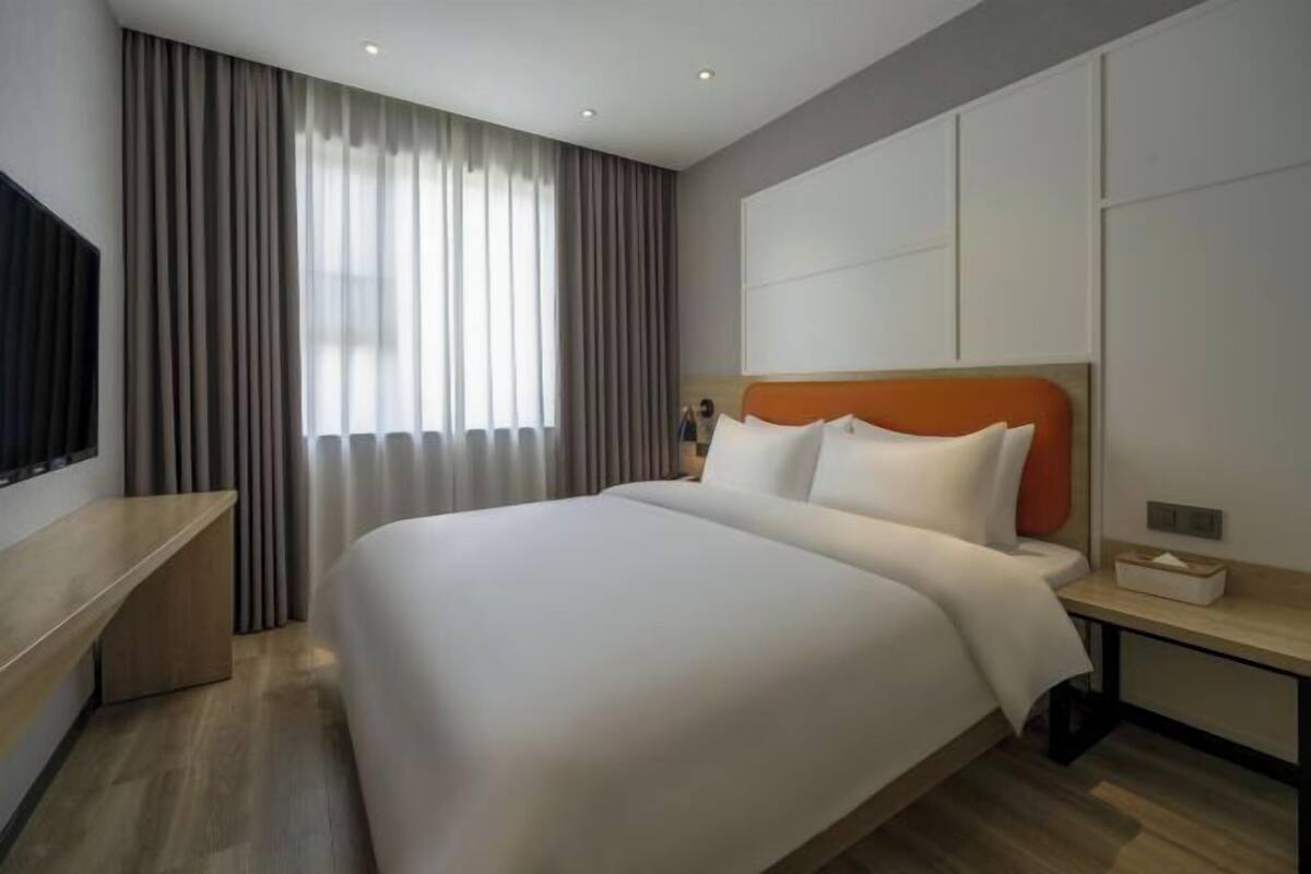 A modern hotel room with a large bed, a bedside table, a TV, and a window with curtains.