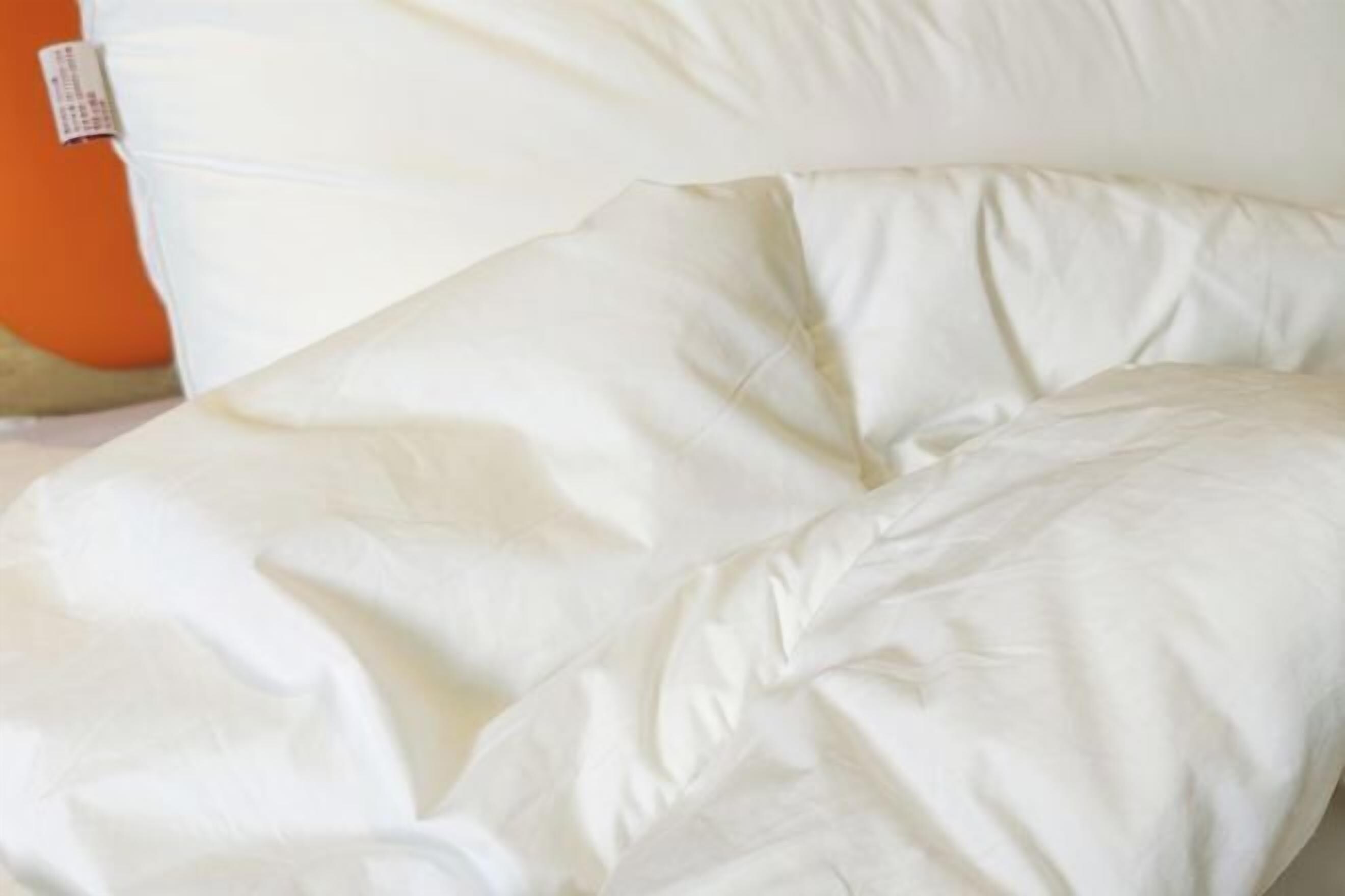 Un lit avec une literie blanche et un oreiller, une étiquette et un objet orange.