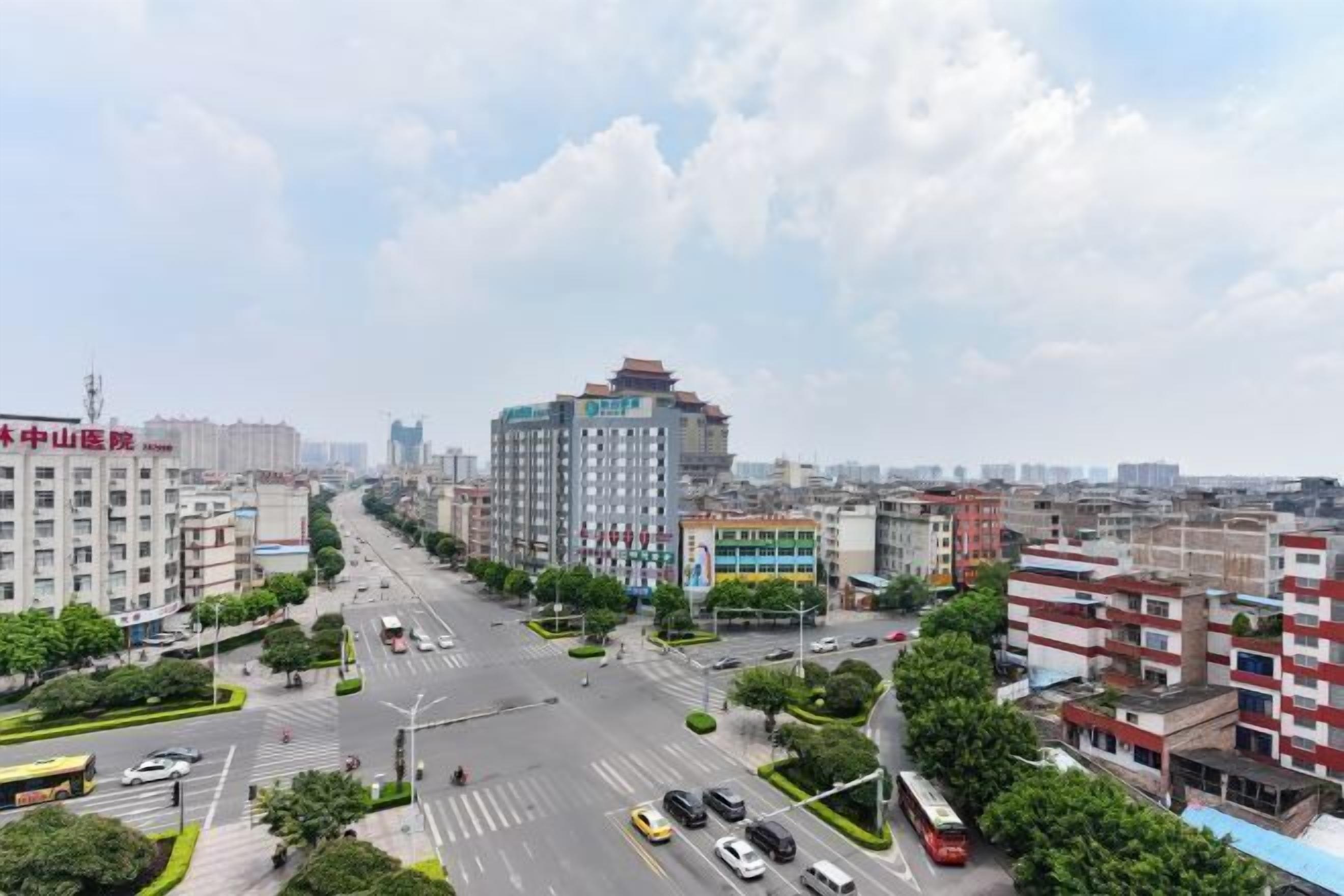 A cityscape with a prominent building in the center, surrounded by other buildings and a wide road with vehicles.