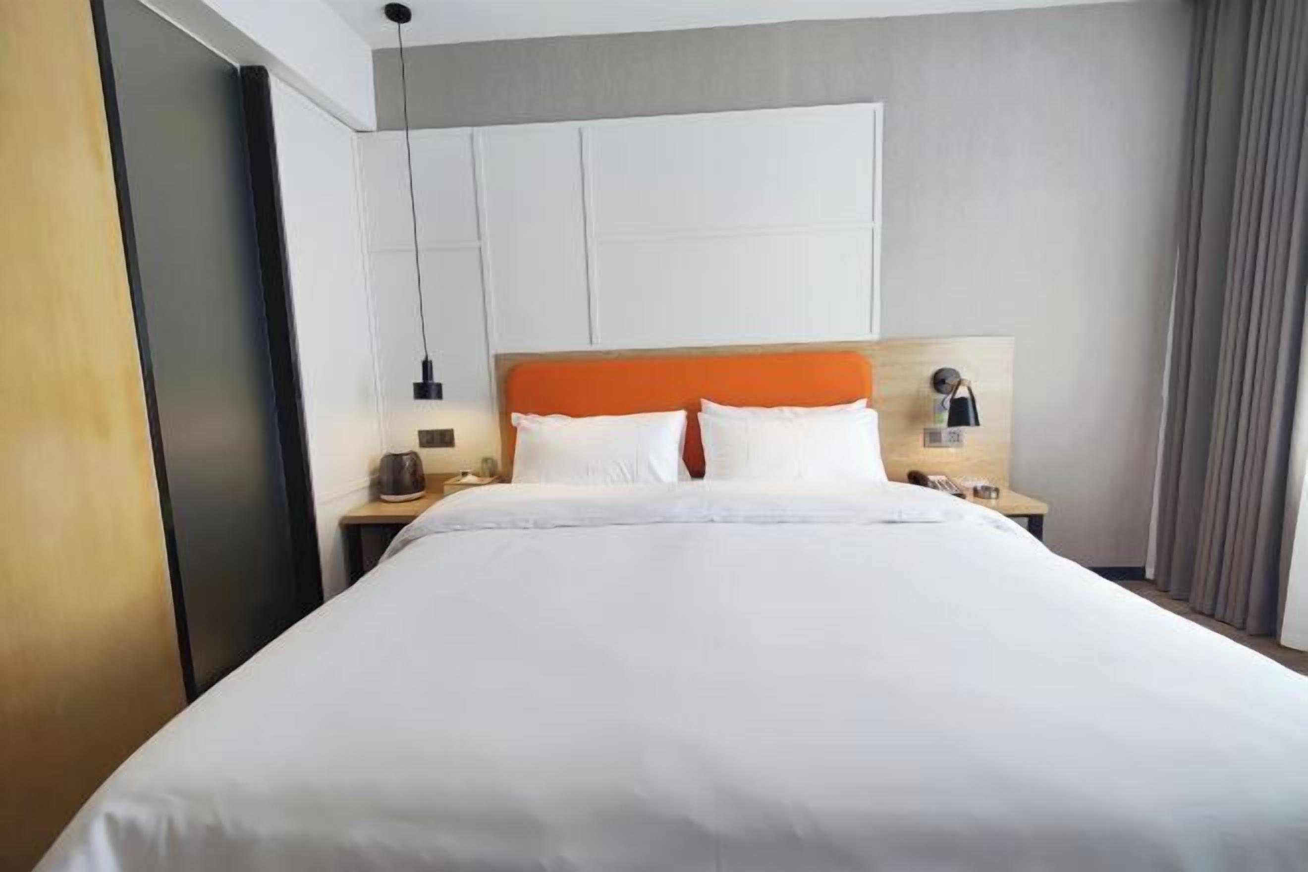 A hotel room with a large bed, a wooden headboard, a nightstand with a lamp, and a wall-mounted panel.