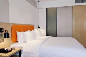 A modern hotel room with a wooden headboard, white bedding, a bedside table with a phone, and a wall-mounted light. - Qianyi Yicheng Hotel (Yulin Shizi Street Yuntian Palace) (Yulin)