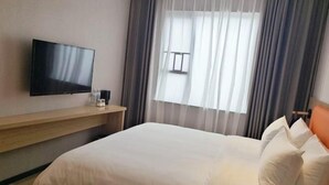 A hotel room with a bed, a flat-screen TV mounted on the wall, a bedside table with a lamp, and a window with curtains. - Qianyi Yicheng Hotel (Yulin Shizi Street Yuntian Palace) (Yulin)