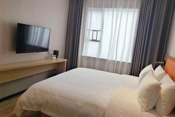 A hotel room with a bed, a flat-screen TV mounted on the wall, a bedside table with a lamp, and a window with curtains. - Qianyi Yicheng Hotel (Yulin Shizi Street Yuntian Palace) (Yulin)