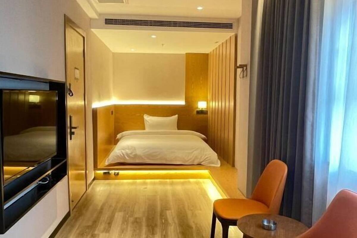 A modern hotel room with a bed, a television, a seating area, and a view of the outside.