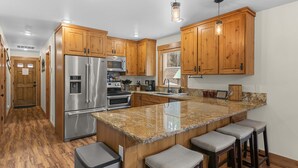 A kitchen with wooden cabinets, stainless steel appliances, granite countertops, and bar stools. - River's Bend Lodge- Hot Tub, Fire Pit, Games & Ski (Leavenworth)