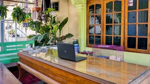 A wooden desk with a laptop, surrounded by potted plants and a window with a view. - OYO 92359 Kost Maluku 36 Family Residence (Kanigoro)
