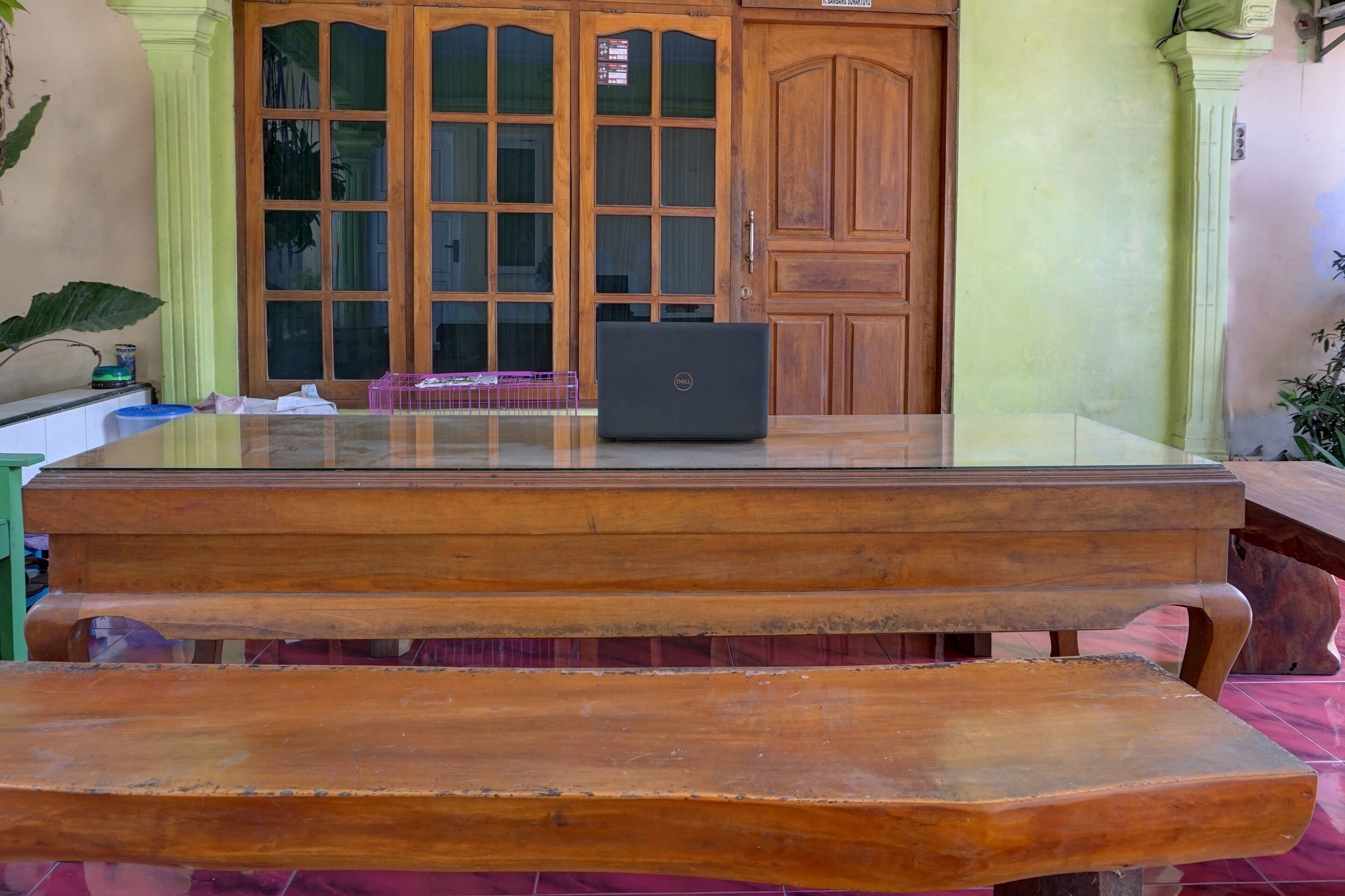 A wooden table with a laptop, a green door, and a pink tablecloth.